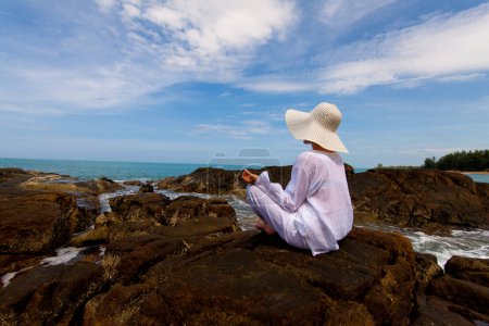 Foto de Pintoresca foto de mujer joven con ropa blanca y sombrero pasar tiempo en la playa durante las vacaciones - Imagen libre de derechos