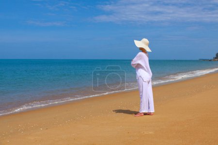 Photo for Scenic shot of young woman with white clothes and hat spending time at beach during vacation - Royalty Free Image
