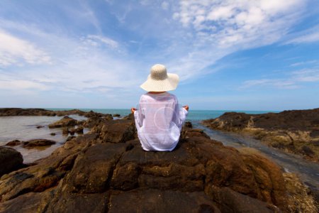 Photo for Scenic shot of young woman with white clothes and hat spending time at beach during vacation - Royalty Free Image