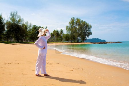 Foto de Pintoresca foto de mujer joven con ropa blanca y sombrero pasar tiempo en la playa durante las vacaciones - Imagen libre de derechos