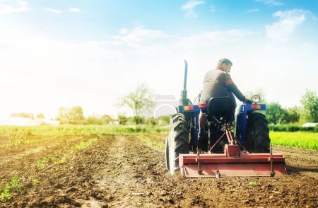 "Farmer on a tractor with milling machine loosens, grinds and mixes soil. Cultivation technology equipment. Loosening the surface, cultivating the land for further planting. Farming and agriculture."