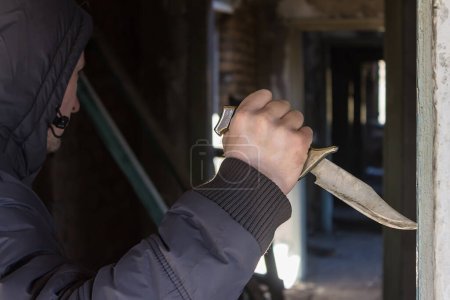 Foto de Un matón con un cuchillo en la mano está cazando en una habitación oscura - Imagen libre de derechos