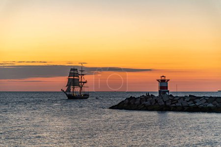 Photo for Tall ship, vessel, sailing and preparing the enter inside the harbor of Scheveningen at the vivid sunset moment, The Hague, Netherlands - Royalty Free Image