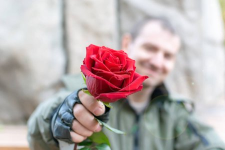 Photo for Hand of a man in leather gloves gives a red rose flower - Royalty Free Image