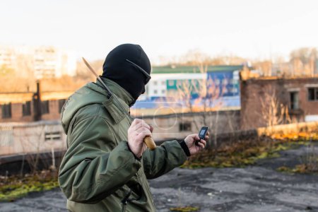 Téléchargez les photos : Criminel avec un gros couteau regarde dans le téléphone - en image libre de droit