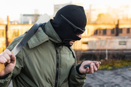 Foto de Criminal en una máscara en una rabia mira el teléfono - Imagen libre de derechos