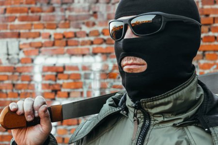 Foto de Comando en una máscara y gafas con un machete en la mano contra una pared de ladrillo - Imagen libre de derechos