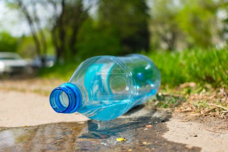 Téléchargez les photos : Pollution environnementale par les bouteilles en plastique. Une bouteille en plastique se trouve sur le trottoir dans un parc - en image libre de droit