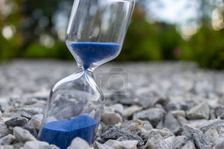 Photo for Hourglass with beautiful blue sand lie on small stones - Royalty Free Image