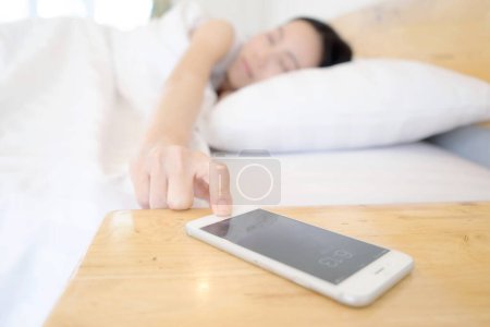 Téléchargez les photos : Sommeil femme être réveillé par téléphone portable dans la chambre - en image libre de droit