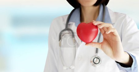 Photo for Positive female doctor standing with stethoscope and red heart - Royalty Free Image