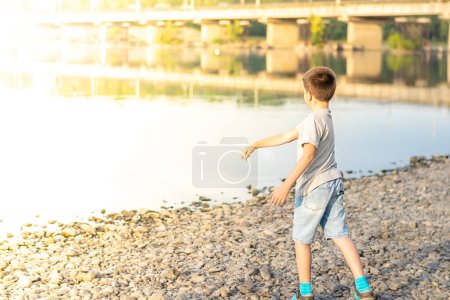 Photo for A child, a teenager, on a stony shore throws stones into the river - Royalty Free Image