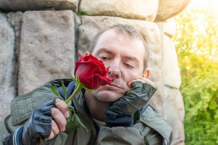 Foto de El tipo se sienta triste y huele un capullo de rosa rojo en su mano - Imagen libre de derechos