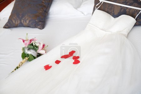 Téléchargez les photos : Fleurs et robe de mariée sur le lit - en image libre de droit
