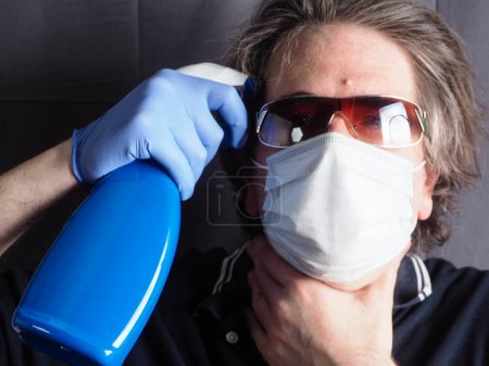 Foto de Divertido humorístico adulto caucásico 40s hombre usando protección quirúrgica máscara y celebración de aerosol botella - Imagen libre de derechos