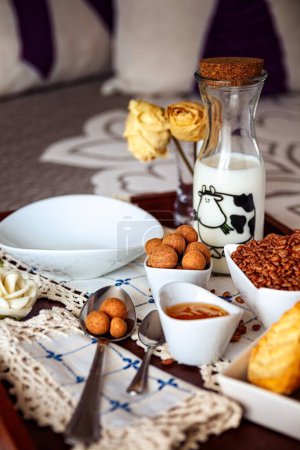 Photo for Tray with continental breakfast on hotel bed made of cereals, Cinnamon Balls, chocolate, cakes and a bowl with spoon. Breakfast in bed. Front view - Royalty Free Image