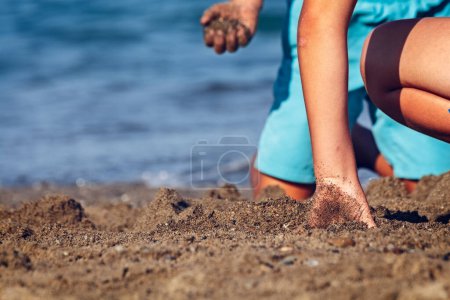 Téléchargez les photos : Garçon faisant des châteaux dans le sable du rivage de la plage. Été - en image libre de droit
