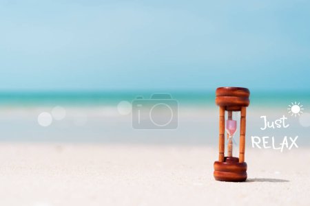 Téléchargez les photos : Juste détendre citation avec sablier sur sable et plage d'été fond bleu ciel. Temps de voyage concept de saison touristique - en image libre de droit