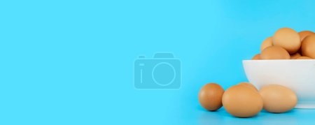 Foto de Fresh chicken eggs in white bowl and chicken eggs on blue background - Imagen libre de derechos