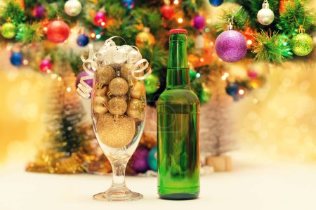 Foto de "bolas de Navidad brillantes en un vaso de cerveza junto a una botella verde y un árbol de año nuevo decorado" - Imagen libre de derechos