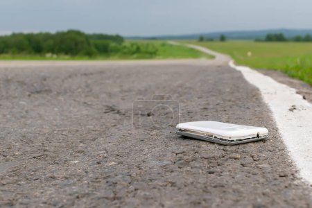 Photo for View of a mobile phone lying on the asphalt on a country road in cloudy weather - Royalty Free Image