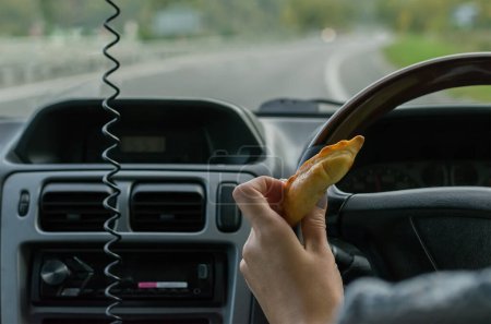 Photo for "Closeup, of female hand holding a bun behind the wheel of the car in motion on highway" - Royalty Free Image
