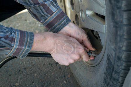 Téléchargez les photos : Mains humaines insérer le tuyau de la pompe de voiture pour pomper l'air dans la roue de la voiture - en image libre de droit