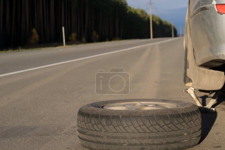 Téléchargez les photos : Spare wheel lying near the car. The car is mounted on the Jack - en image libre de droit