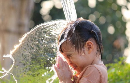 Téléchargez les photos : Cute asian little child girl having fun to play with water spraying hose in summer garden. - en image libre de droit
