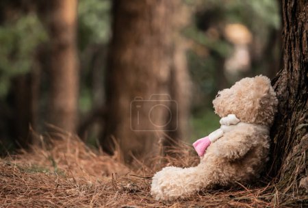 Photo for The teddy bear sits on the floor, sitting against the tree. Emotional and expression concept. - Royalty Free Image