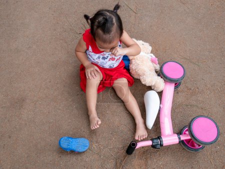 Téléchargez les photos : Asiatique petite fille assis sur le sol après être tombé et se blesser au genou - en image libre de droit
