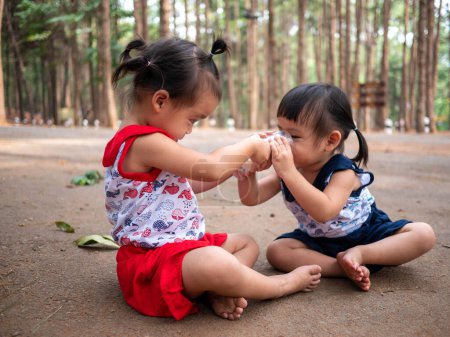 Téléchargez les photos : Asiatique petit enfant assis dans le jardin et donner un peu de lait à sa sœur de verre - en image libre de droit