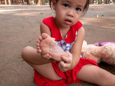 Photo for Asian little girl sitting on the ground after falling and getting hurt at heel - Royalty Free Image