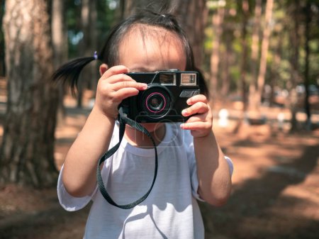 Foto de "Feliz niño asiático sosteniendo con la cámara y sonreír cara en el bosque de pinos, Tailandia. Jugar es aprender para los niños." - Imagen libre de derechos