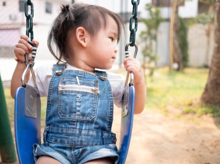 Téléchargez les photos : Asiatique petit enfant est assis sur une balançoire heureusement dans la cour de récréation. Jouer, c'est apprendre pour les enfants. Photo noir-blanc - en image libre de droit