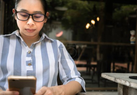 Photo for Stressed Asian women sitting on wooden chair with smartphone in coffee cafe. Health and medical concept - Royalty Free Image