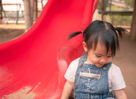 Photo for "Asian little girl sitting on the sand ground in the playground and playing a sand with smile happily. Playing is learning for children." - Royalty Free Image