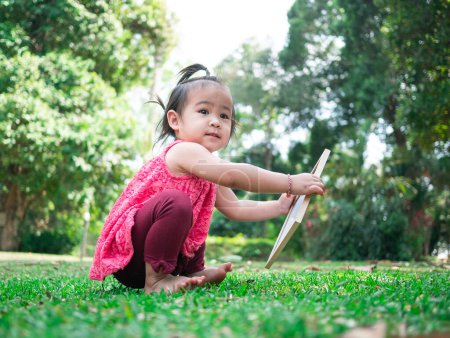 Photo for Asian little girl holding empty white board and sitting on grasses ground. - Royalty Free Image