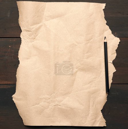 Photo for "black pencil and untwisted brown paper on a wooden surface from " - Royalty Free Image