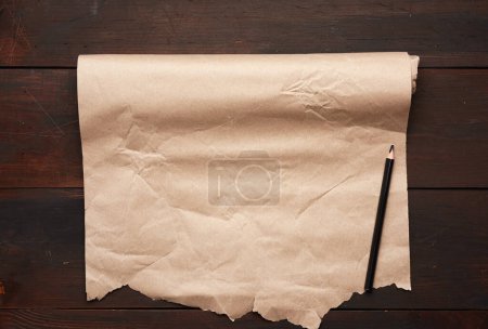 Téléchargez les photos : Crayon noir et rouleau de papier brun non torsadé sur une surface en bois - en image libre de droit