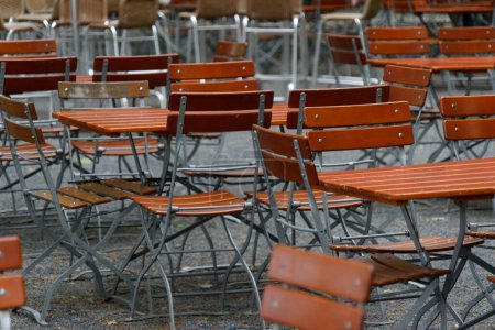 Téléchargez les photos : Chaises et tables Unoccupied dans un restaurant de jardin avec pieds de table et pieds de chaise en fer et dessus en bois - en image libre de droit