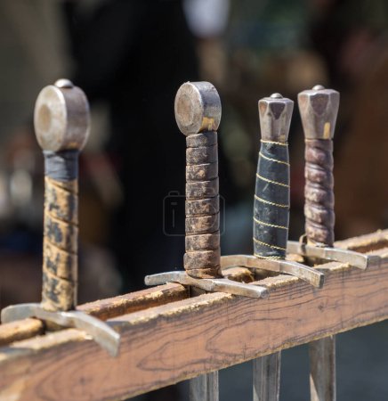 Foto de Manijas de espadas históricas colgadas en fila en un mercado medieval - Imagen libre de derechos