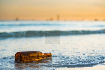 Téléchargez les photos : Bouteille en verre brun sur la plage de Tawaen à l'aube, le soleil se levait - en image libre de droit