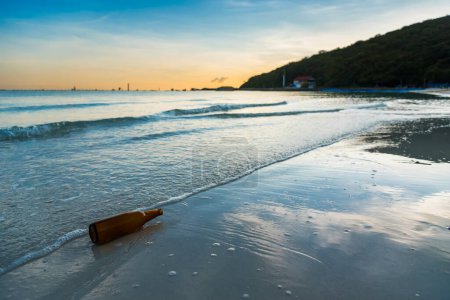 Téléchargez les photos : Bouteille en verre brun sur la plage de Tawaen à l'aube, le soleil se levait - en image libre de droit
