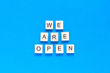 Téléchargez les photos : "We are open. Wooden cubes with a text message We are open on a blue background. The view from the top. Flat layout. An office, cafe, or store welcomes guests after a coronavirus outbreak." - en image libre de droit