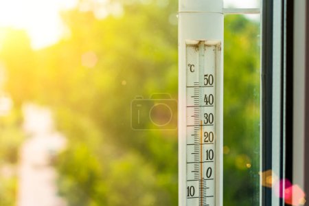 Téléchargez les photos : Le thermomètre à l'extérieur de la fenêtre montre une température de l'air très chaude, chauffée par les rayons du soleil brillant - en image libre de droit