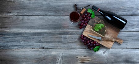Foto de Vino tinto con cuña de queso más hojas de albahaca y uvas sobre fondo rústico - Imagen libre de derechos