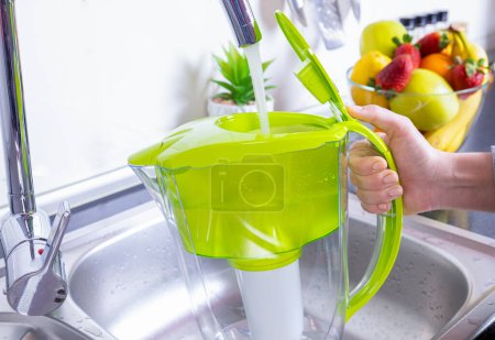 Téléchargez les photos : Femme remplissant cruche filtre à eau dans la cuisine - en image libre de droit