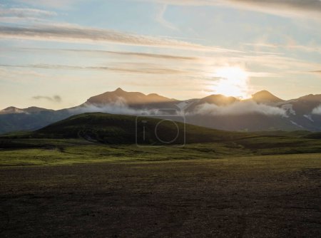 Foto de Salida del sol en el camping Alftavatn con montañas cubiertas de nieve y verdes colinas. Paisaje de la Reserva Natural de Fjallabak en las tierras altas de Islandia - Imagen libre de derechos