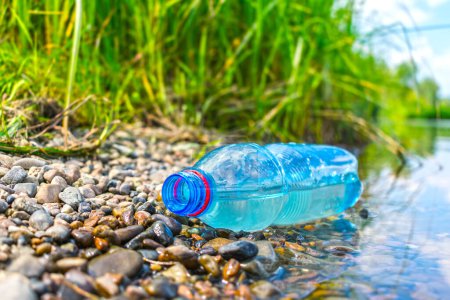 Téléchargez les photos : Le problème de la pollution de l'environnement par le plastique. Une bouteille en plastique jetée sur la rive - en image libre de droit